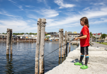 Profile of boy in red shirt and green crocs fishing Perkins Pier on a sunny day. 