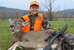 Young boy wearing orange vest and holding deer he harvested