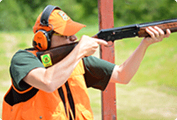 guy in orange vest and hat shooting a shotgun