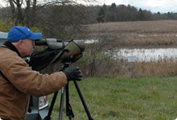 man looking through a spotting scope over a wetland